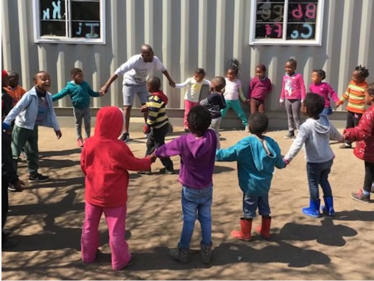 Children and a volunteer holding hands in a circle outside an orphanage